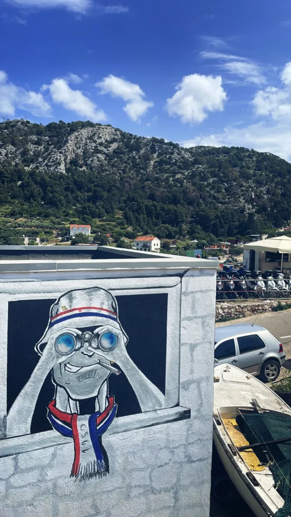 Graffiti mural Torcida Split en costa dálmata: ilustración de hincha con gorro bucket hat, prismáticos y bufanda 1950 del Hajduk Split vigilando el territorio.