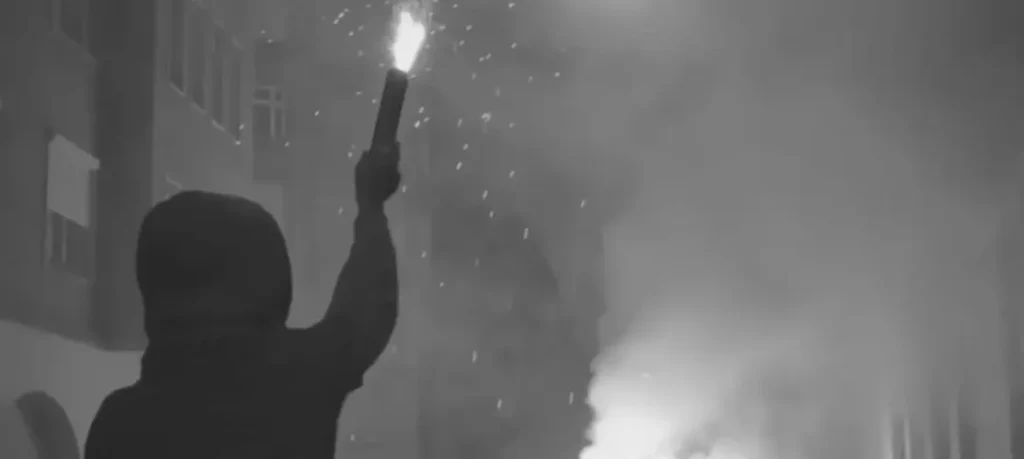 Fotografía en blanco y negro de un niño en hombros sosteniendo una bengala durante el corteo de los Hooligans Hungría.