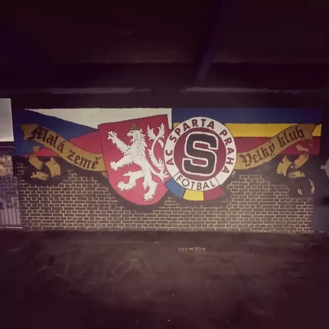 mural-ultras-sparta-praga Graffiti sobre pared de ladrillo que muestra el escudo del león de la República Checa junto al logo del AC Sparta Praga y una cinta con el lema en checo "Malá země Velký klub" sobre los colores del equipo.