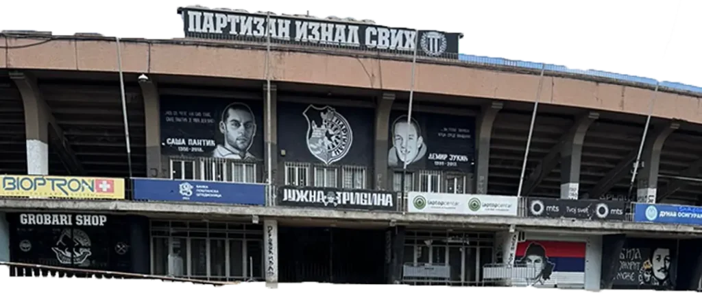 partizan-stadion Fachada exterior del Estadio JNA del Partizan de Belgrado con murales de seguidores fallecidos, la Grobari Shop y el lema "Partizan por encima de todos" en cirílico.