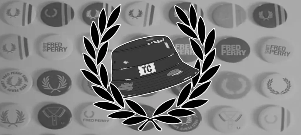Emblema de Territorio Casual: un sombrero de cubo negro con parche TC rodeado por la corona de laurel de Fred Perry, sobre un fondo de pines de la marca.